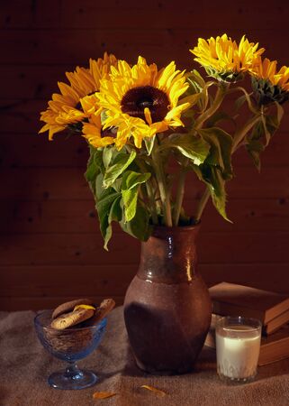 Bouquet of sunflowers in a clay jug on the table on the wooden background. Still life in rustic style.の写真素材
