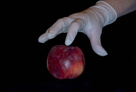 A woman's hand in a rubber glove and a red Apple on a black background.の写真素材