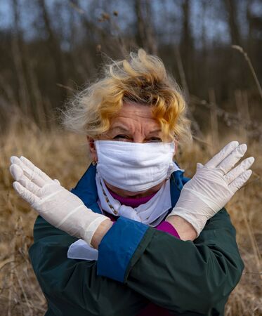An elderly woman in a medical protective mask and rubber gloves gestures stop coronavirus. Concept photo symbolizing the end of the coronavirus epidemic. Focus on the gloved hand.の写真素材