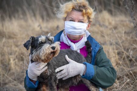 An elderly woman in a protective medical mask and rubber gloves on a walk with a dog.