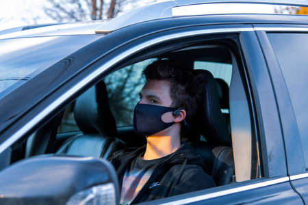 Moscow region, Russia, April 2020. A young man in a medical mask is sitting at the wheel of a car.のeditorial素材