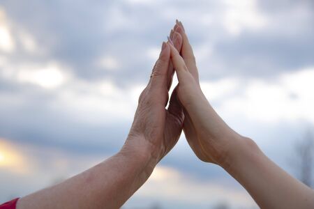 The hand of an elderly woman and the hand of a teenage girl on the background of a cloudy sky.の写真素材