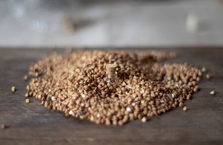 Picture with soft focus of tiny corked glass jar with buckwheat in a pile of spilled buckwheat. Concept of healthy nutrition, diet, vegetarian products. Nutrition. Selective focus.の写真素材