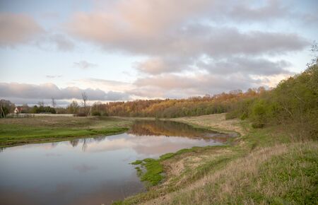 Spring evening landscape. River, field and forest, illuminated by the sunset rays of the sun.