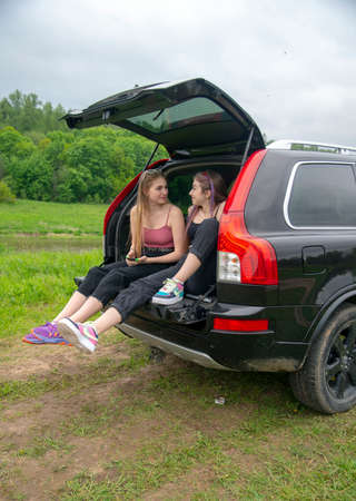 Two teenage girls are sitting in the trunk of a car with a mobile phone.のeditorial素材