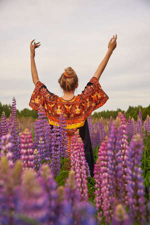 A girl stands in a lupine field with her hands up and her back to the camera.の写真素材