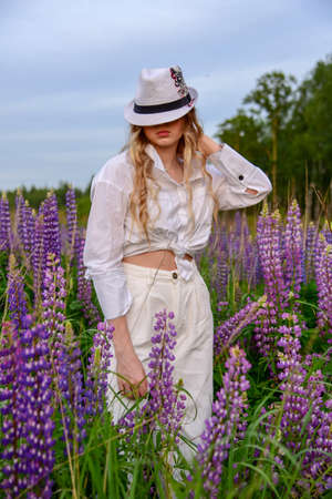 A girl with long blond hair, poses against a background of blooming lupines.の写真素材