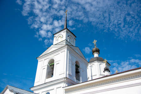 A white bell tower with a spire and cross against a bright blue sky.の写真素材