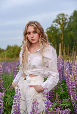 A girl with long blond hair, poses against a background of blooming lupines.の写真素材