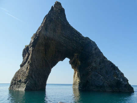 A triangular rock with an arch in the middle protrudes from the sea.の写真素材