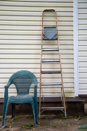 A stepladder and a plastic garden chair stand against the wall.の写真素材