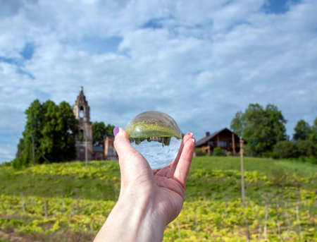 Glass ball in a woman's hand with a bright manicure. The old dilapidated Church is reflected in the lens.の写真素材