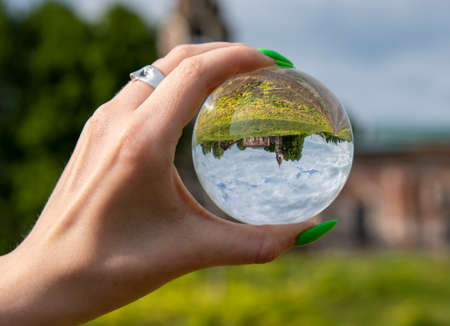 Glass ball in a woman's hand with a bright manicure. The old dilapidated Church is reflected in the lens.の写真素材