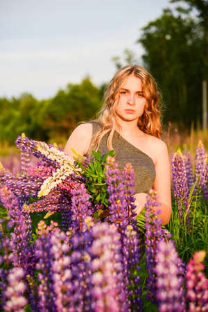 A young girl with long blonde wavy hair poses for the camera with a large bouquet of lupins.の写真素材