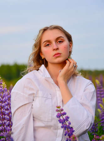 A girl with long blond hair, in a white shirt, poses against a background of blooming lupine fields.の写真素材
