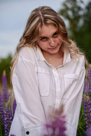 A girl with long blond hair, in a white shirt, poses against a background of blooming lupine fields.の写真素材