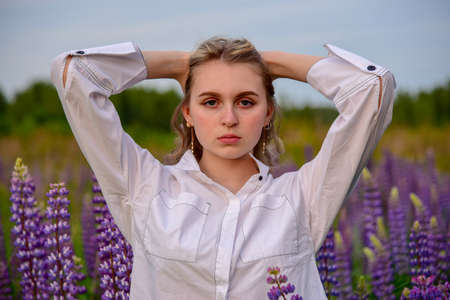 A girl with long blond hair, in a white shirt, poses against a background of blooming lupine fields.の写真素材
