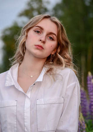 A girl with long blond hair, in a white shirt, poses against a background of blooming lupine fields.の写真素材