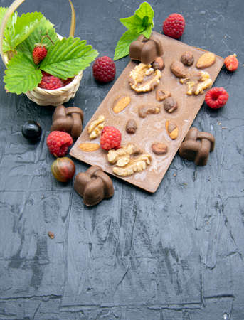 Chocolate bars, various ripe berries and mint leaves lie on a black slate background. Advertising of confectionery, copy space for text.の写真素材