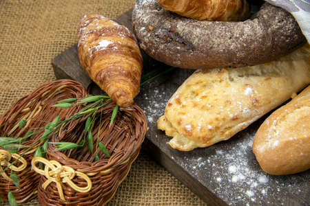 Several types of bread lie on a rough wooden Board against the background of matting. Advertising bakery products, copy space for text.の写真素材