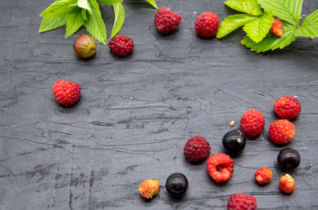 Ripe fresh berries and mint leaves lie on a black slate background. Copy space for text, design.の写真素材