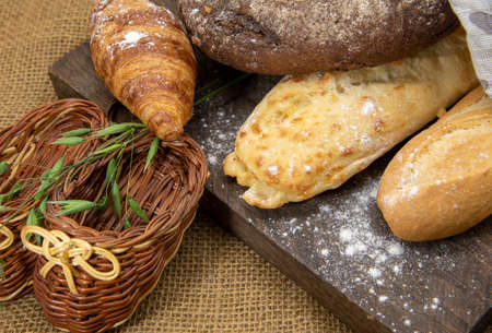 Several types of bread lie on a rough wooden Board against the background of matting. Advertising bakery products, copy space for text.の写真素材