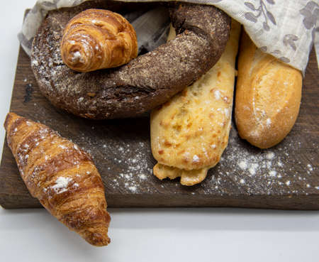 Several types of bread lie on a rough wooden Board on light background. Advertising bakery products, copy space for text.の写真素材