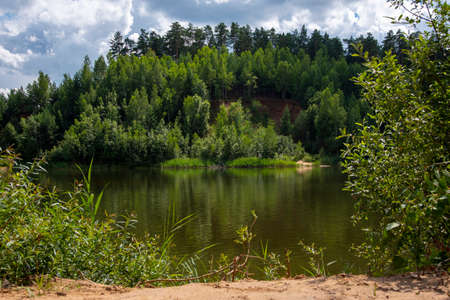The lake is surrounded by green forests. Trees reflect in the water and turn it green. Summer landscape.の写真素材