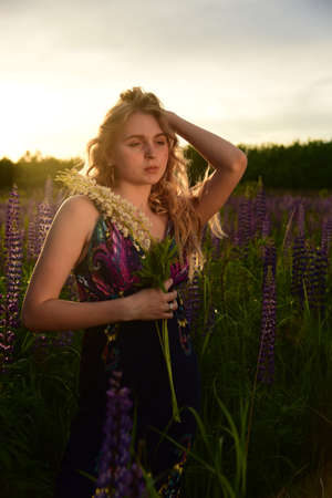 A blonde girl with long hair with a flower in her hands is illuminated by the rays of the outgoing sun.の写真素材