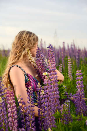 A charming blonde girl with long wavy hair poses in a field with bright lupines.の写真素材