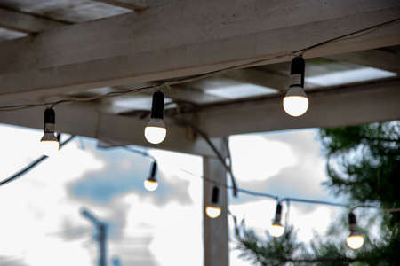A garland of burning light bulbs hangs under the wooden ceiling of the summer porch.の写真素材
