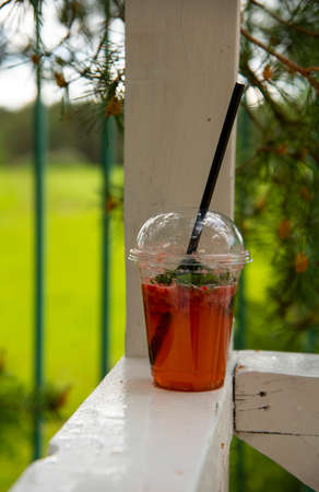 A single-use plastic glass with a refreshing drink stands on a wooden crossbar.の写真素材