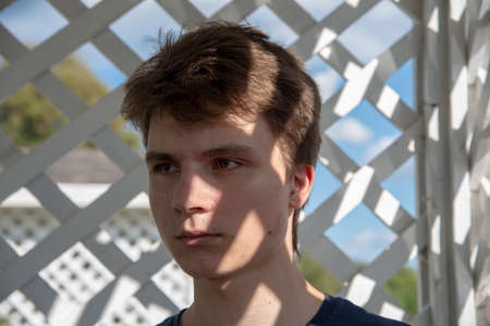 Portrait of a thoughtful young man with graphic shadows on his face from a wooden garden grating.の写真素材