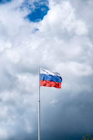 Russian tricolor flag waving in the wind against a cloudy sky.Vertical photo.