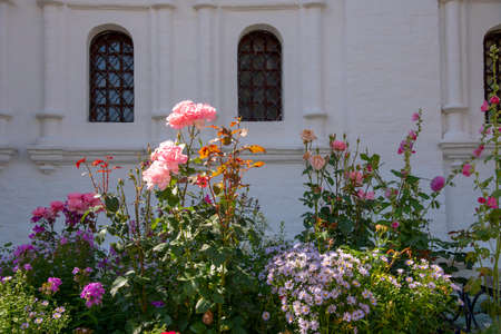 A flowerbed with bright flowers against a white monastery wall with arched Windows.の写真素材