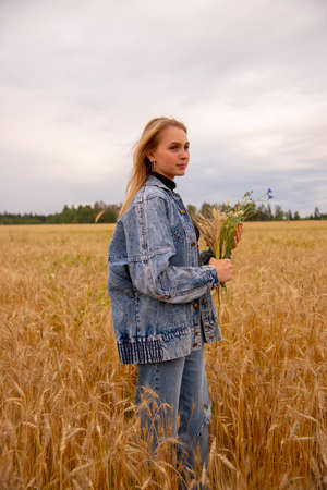 Portrait of a young girl with long blond hair with a bouquet in her hands in a field of rye.