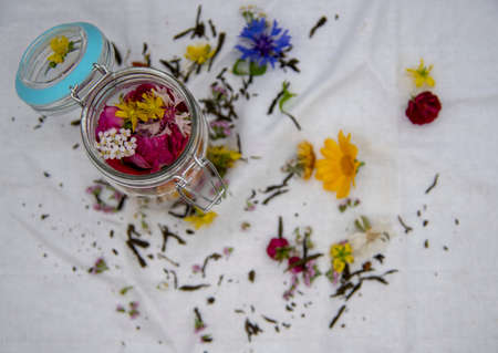 Focus on flowers in a jar. Fresh aromatic medicinal herbs in a glass container on a white linen tablecloth.の写真素材