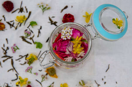 Fresh aromatic medicinal herbs in a glass container on a white linen tablecloth.の写真素材