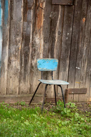 A single battered wooden chair stands on the ground against a plank wall.の写真素材