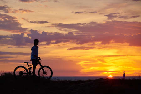 Silhouette of a young man with a Bicycle against the background of a bright colorful sunset.の写真素材