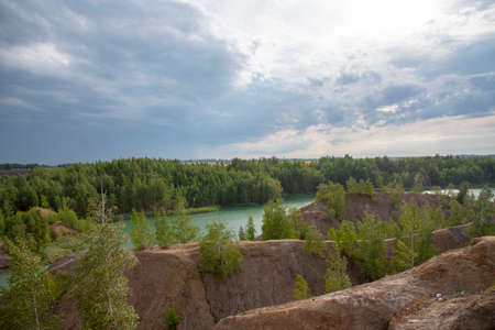 Green lake among sandy relief hills under a cloudy sky.の写真素材