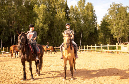 Russia, Moscow region, July 2020. Two teenage girls sit on horses in a training arena on a bright Sunny day.のeditorial素材