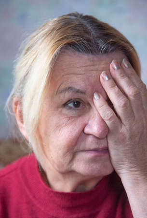 Portrait of an elderly tired woman holding her head with her hand.