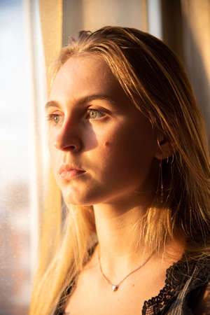 Portrait of a beautiful girl with blonde hair down by the window.の写真素材