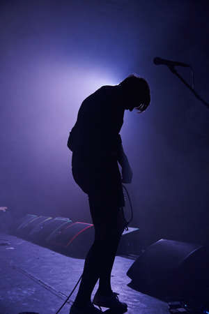 A slightly blurred silhouette of a young man with a guitar in the smoke, illuminated by a contour...