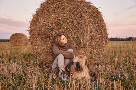 A beautiful sad blonde girl and a dog are sitting in a field.の写真素材
