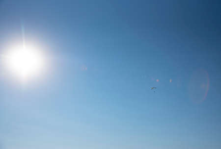 Full frame blue sky, bright disk of the sun and a small silhouette of a paraglider. Copy space for...