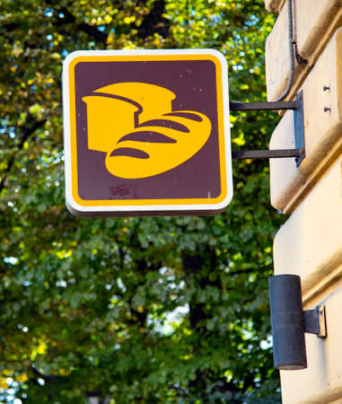 A square bright sign with bread painted on it hangs on the corner of the building.の写真素材