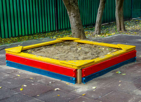 Bright multi-colored children's sandbox on the Playground next to the green fence.の写真素材