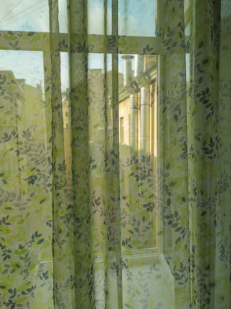 Room window, covered with a light colored curtain. The sun's rays break through the tulle.の写真素材